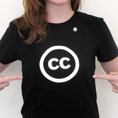 Color photo of a person with long hair, pointing to the white CC icon on the black t-shirt they are wearing.