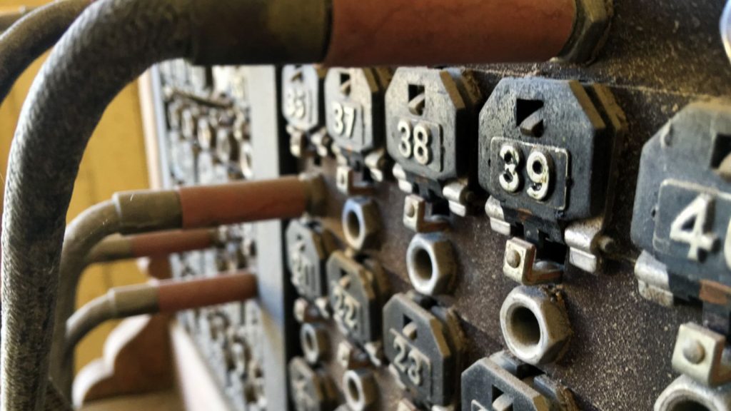 Close up photograph of a vintage telephone switchboard, showing cables plugged into numbered sockets.