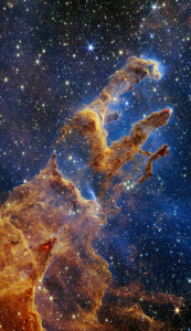 A dramatic image of the Pillars of Creation showing orangish galactic clouds with bright sparkling stars above and shining through from behind.