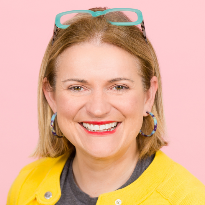 A headshot of Catherine Stihler wearing a bright yellow jacket on a light pink background.