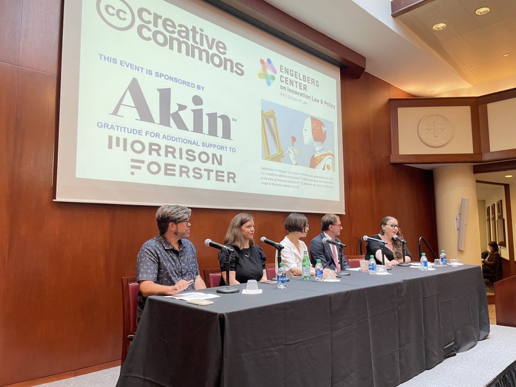 A panel of five people seated at a table on stage below a slide with an image of a robot painting at an empty easel, saying: Creative Commons, Engleberg Center on Innovation Law & Policy, this event sponsored by Akin, gratitude for additional support to Morrison Foerster.