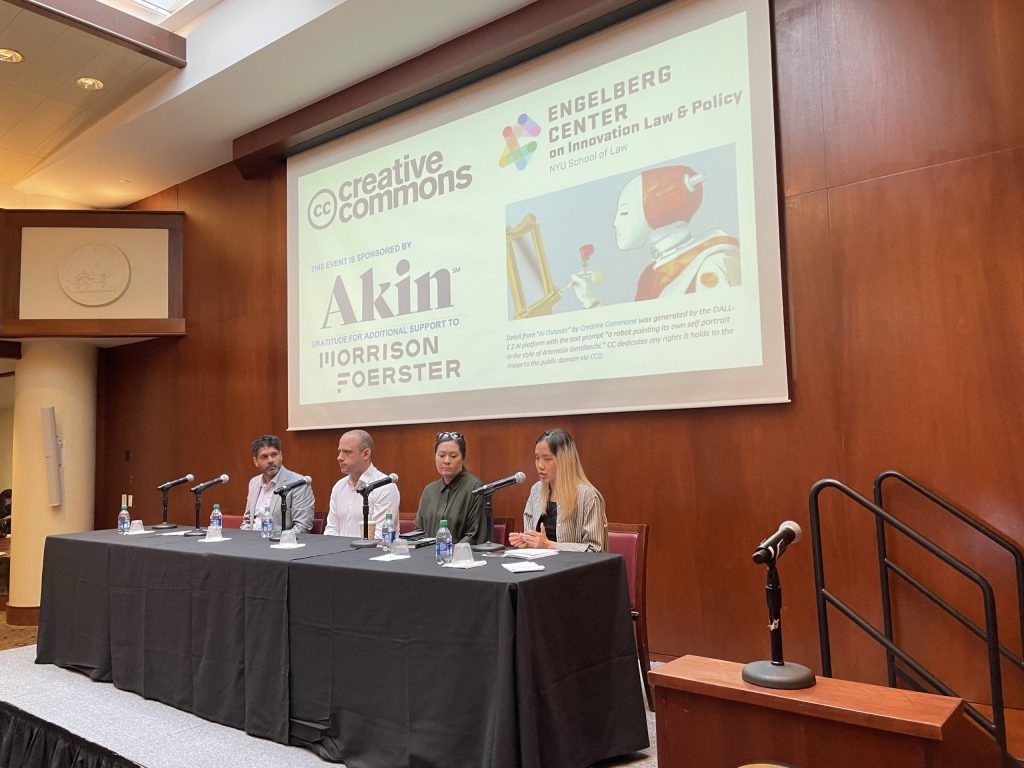 A panel of four people seated at a table on stage below a slide with an image of a robot painting at an empty easel, saying: Creative Commons, Engleberg Center on Innovation Law & Policy, this event sponsored by Akin, gratitude for additional support to Morrison Foerster.