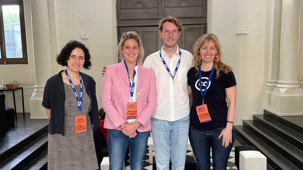 From left to right, the team stands together with GLAM Wiki Lanyards. Jocelyn has short brown curly hair and wears a black and white dress with a black shirt. Brigitte has light brown hair and wears jeans and a pink jacket. Connor wears a white button up shirt and jeans, glasses. Jennryn has long blonde hair and colorful hoop earrings with a CC t-shirt. The team is featured in front of an ornate door and checkered black and white tiled floor.