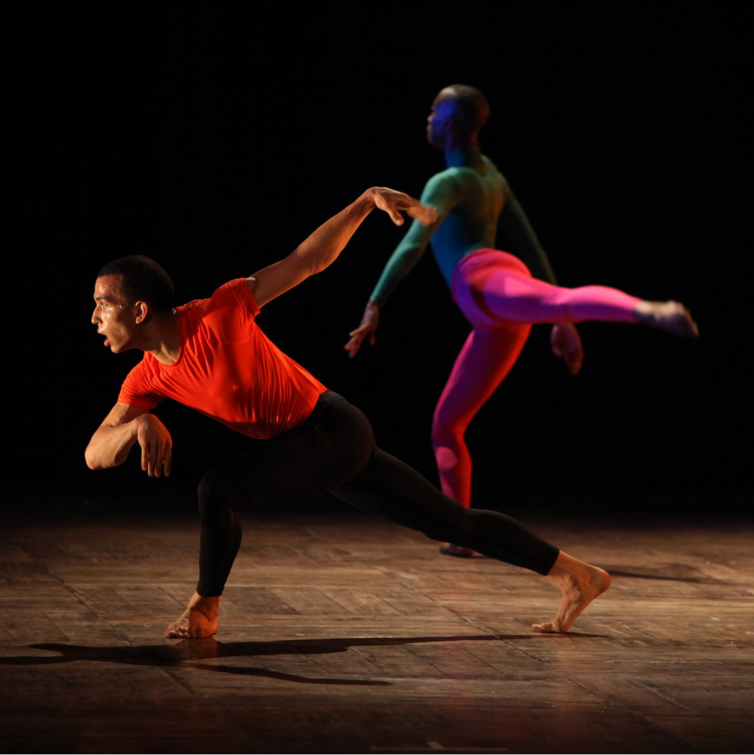 A photo of two dancers lit on a dark stage, taken during a performance from the Spectrum Dance Theater in Dhaka